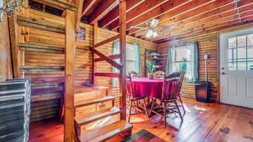 A wooden cabin interior with a dining area, staircase, and a door.