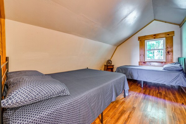 A room with two beds, a wooden ceiling, a window with a view of trees, and a wooden floor.