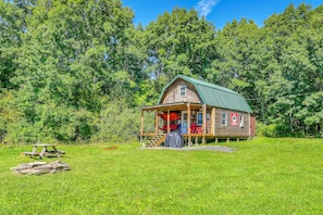 A rustic cabin with a porch, surrounded by lush greenery.