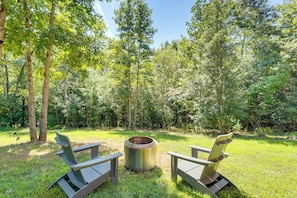 Uma fogueira com duas cadeiras Adirondack numa área gramada, cercada por árvores.