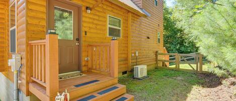 A log cabin with a wooden porch, a front door, and a small step leading to the entrance.