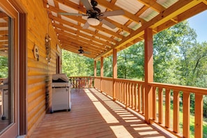Um deck de madeira com ventilador de teto, churrasqueira e vista para uma floresta.