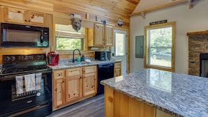 A modern kitchen with wooden cabinetry, a granite countertop, and a stone fireplace. - 4 Mi to Cherokee Lake! Wooded Escape Near Hiking (Murphy)