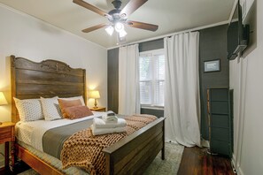 A neatly arranged bedroom with a wooden headboard, a bed with white and patterned bedding, a bedside lamp, a window with curtains, and a ceiling fan. - East Memphis Duplex Near Midtown & Downtown (Memphis)