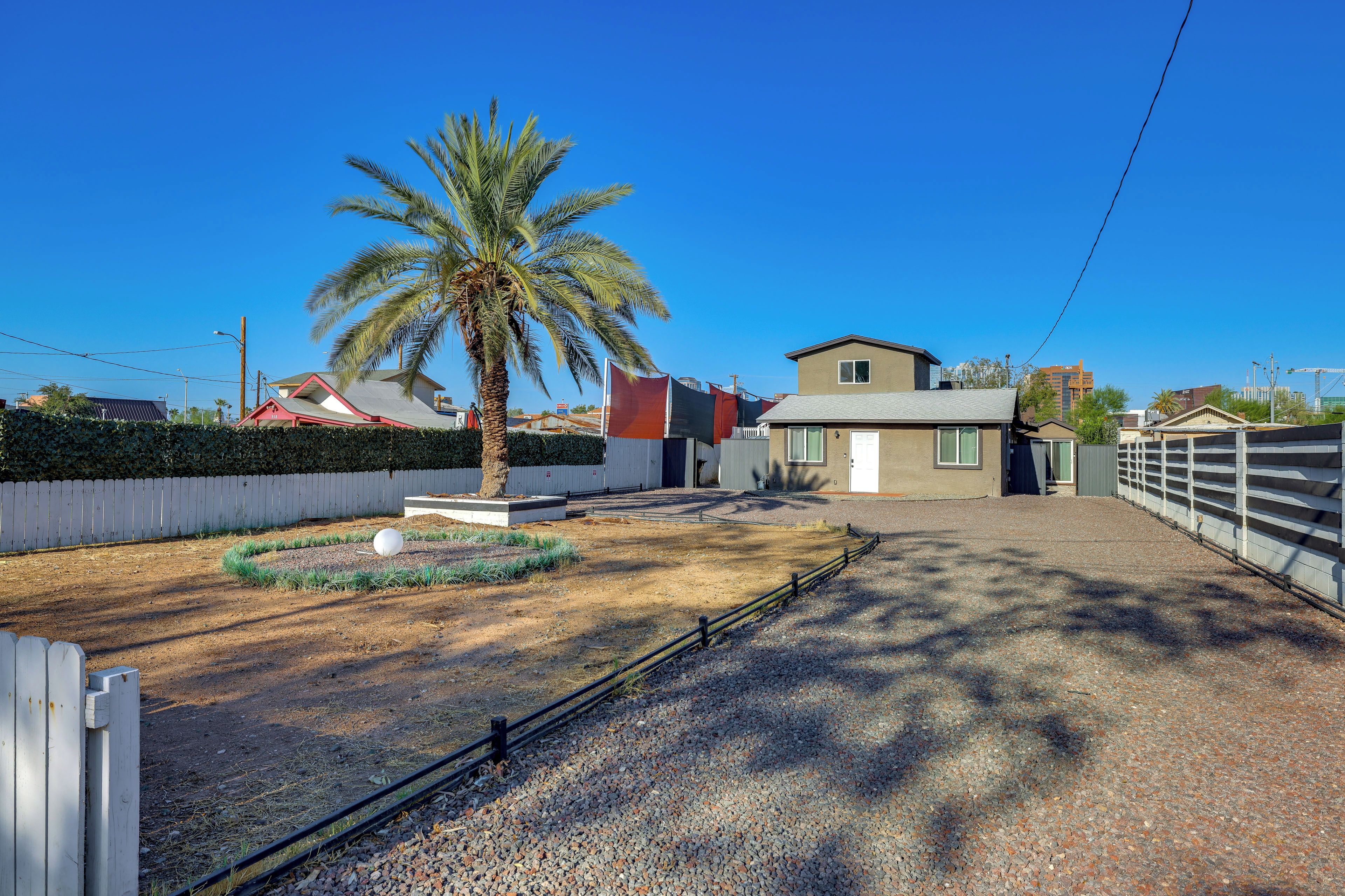 Un barrio residencial con una palmera, un camino de grava y casas con ventanas y puertas visibles.