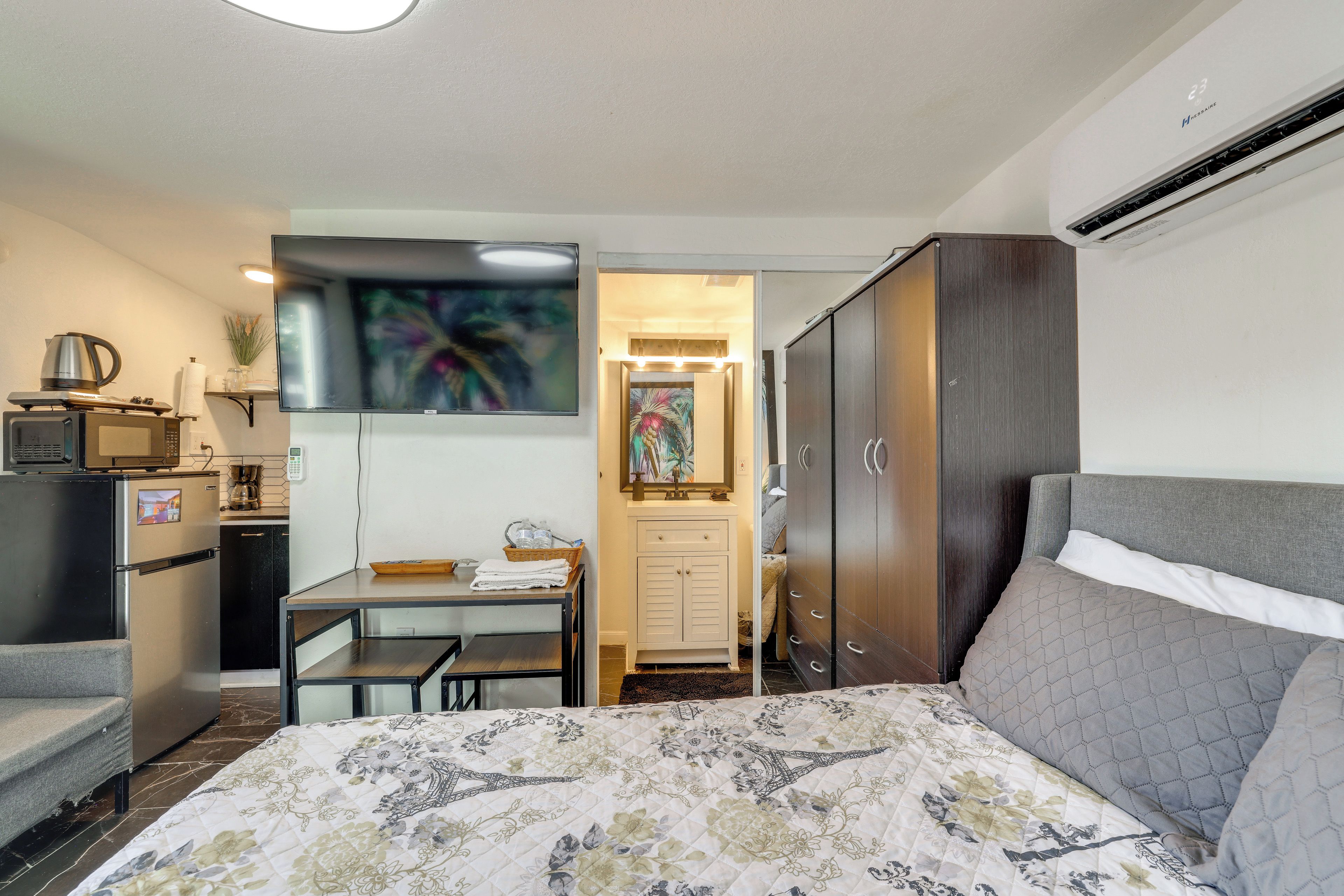 A compact hotel room with a bed, a desk, a wardrobe, and a kitchenette.