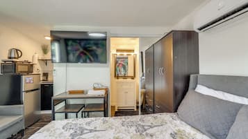 A compact hotel room with a bed, a desk, a wardrobe, and a kitchenette.