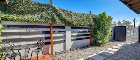 A patio area with a table and chairs, a wall covered with climbing plants, and a gravel pathway.