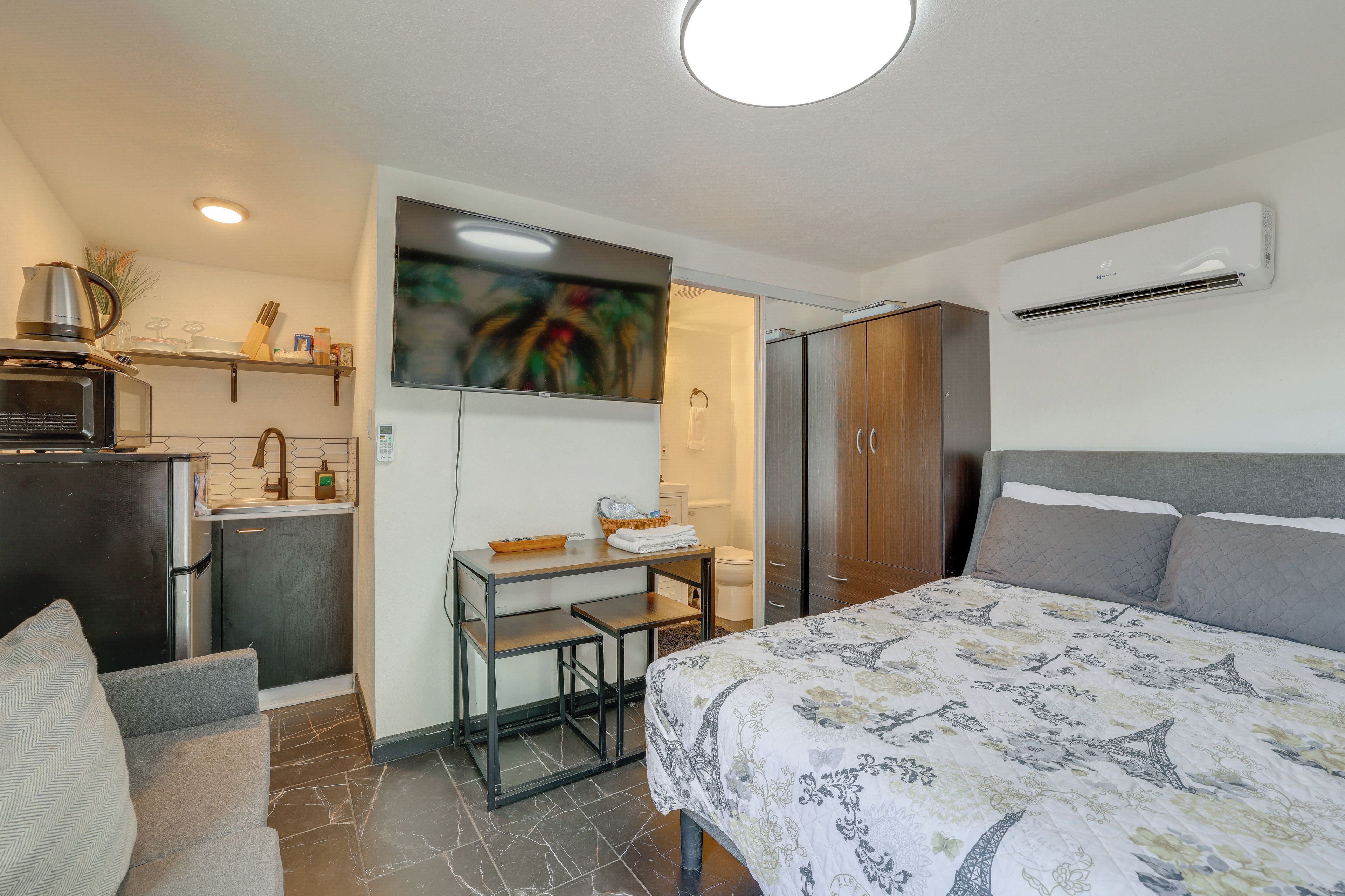 Habitación de hotel compacta con cama, escritorio, kitchenette y armario.