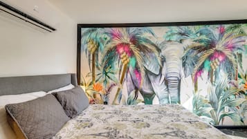 Ein Schlafzimmer mit einem großen Bett, einem grauen Kopfteil und einem farbenfrohen Elefanten-Wandbild.