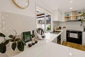 A modern kitchen with white cabinetry, a marble countertop, a kettle, a wine bottle, and a cookbook. - Casa Aqua: Tropical/Coastal Escape & McLaren Vale (Christies Beach)