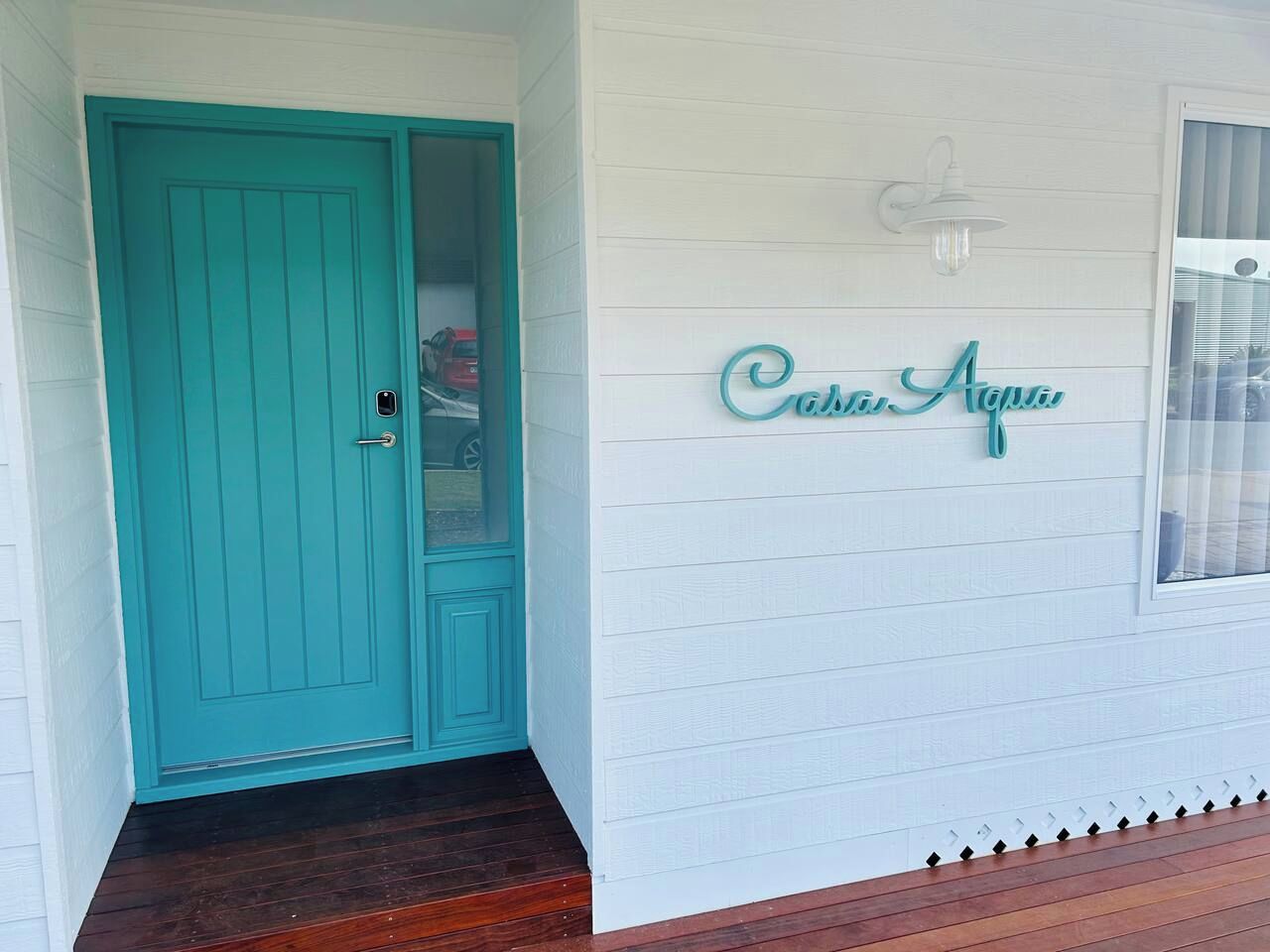 A turquoise door with a small window above it and a sign that reads 'Casa Aqua' on the wall.