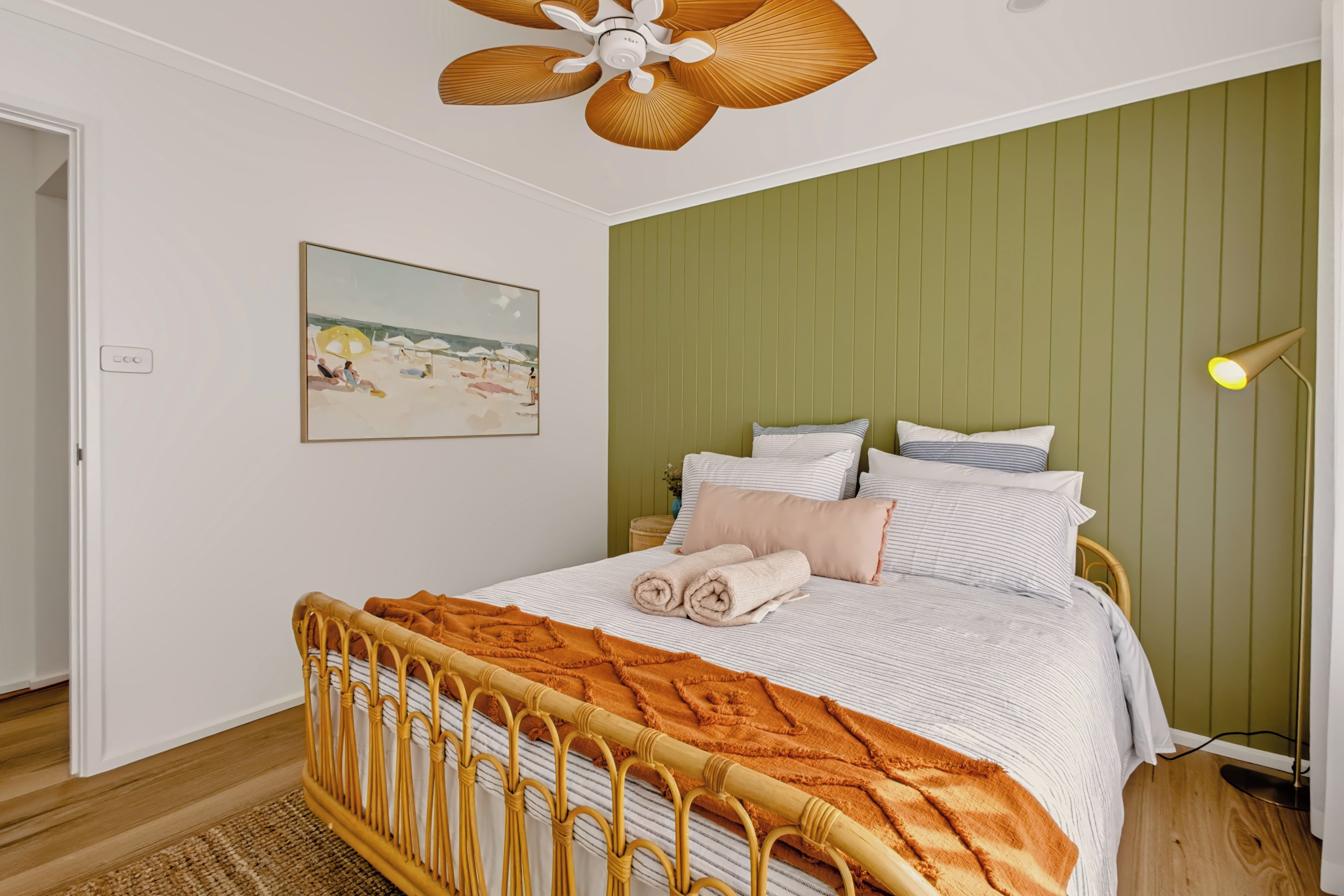 A bedroom with a bed, a painting, a ceiling fan, and a bedside lamp.
