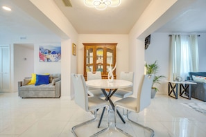 Una sala de estar moderna con comedor, que incluye una mesa redonda y sillas, un sofá y una planta en maceta.