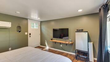A bedroom with a bed, a television, a refrigerator, and a window with curtains.