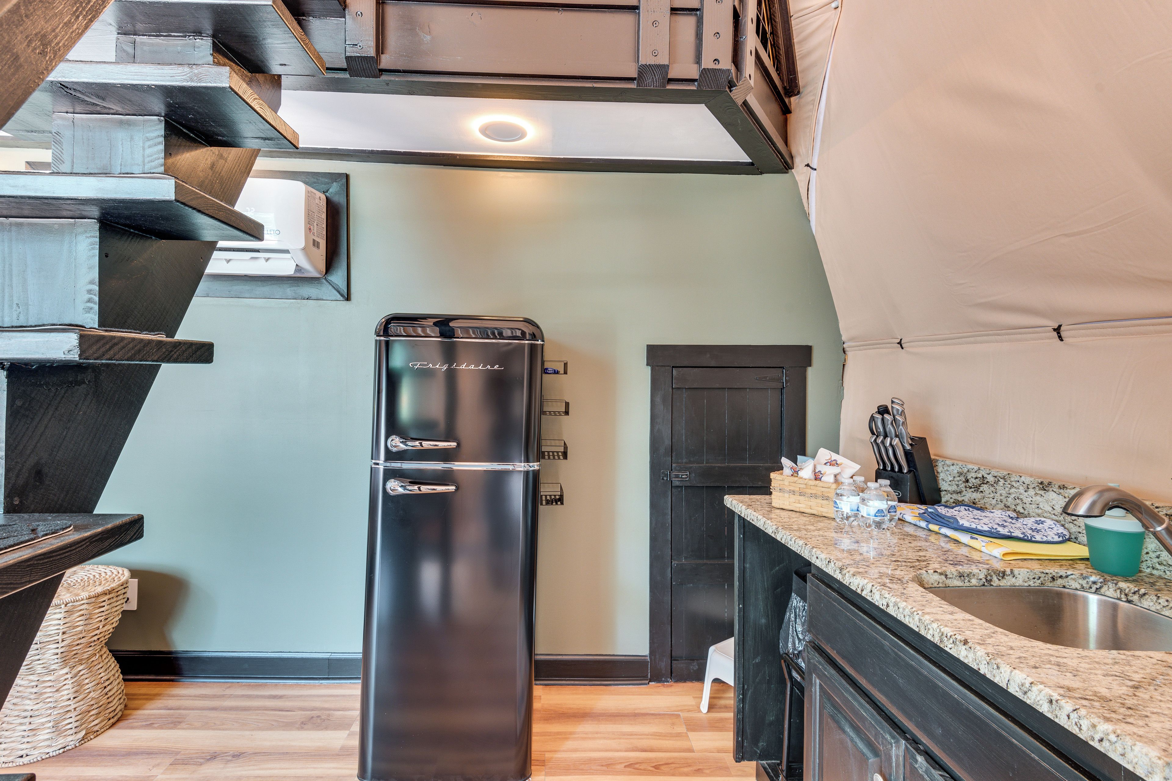 A compact kitchen with a built-in refrigerator, a sink, and a wooden staircase.