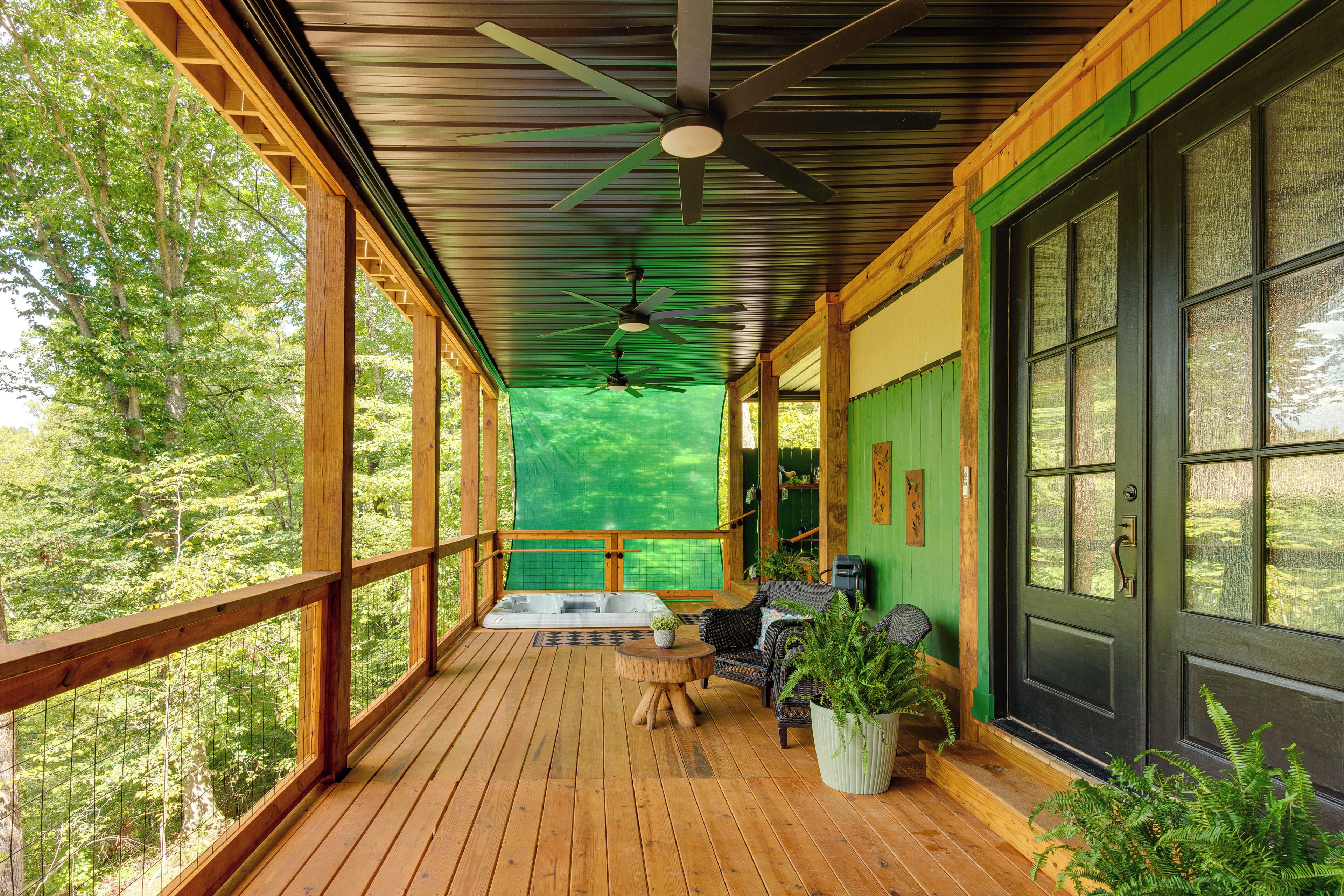 A wooden deck with a hot tub, seating, and a view of the forest.