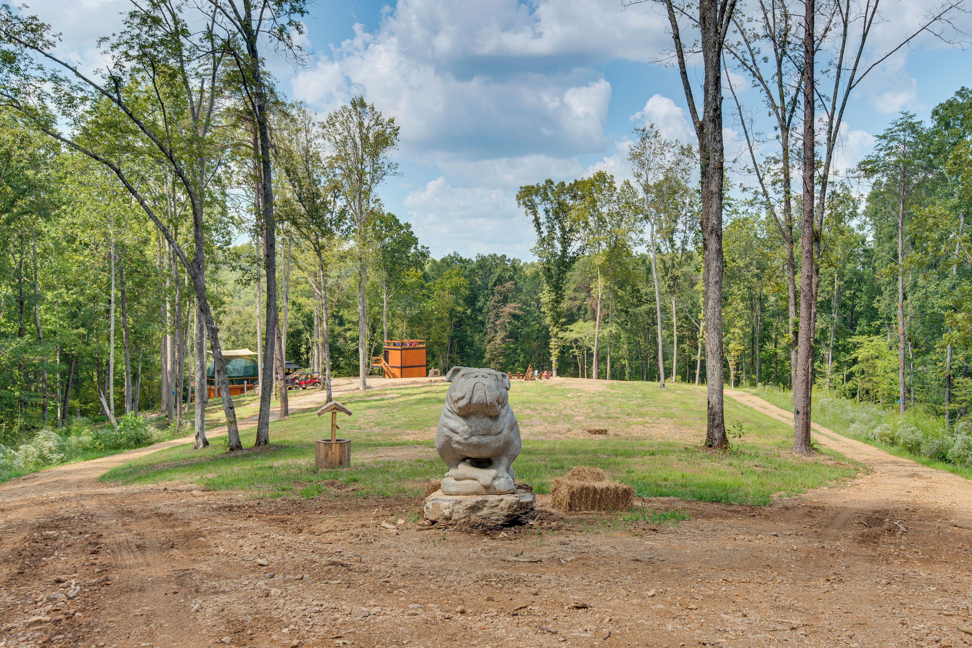 A rustic outdoor area with a dirt path, a stone sculpture, and a wooden structure in the background.