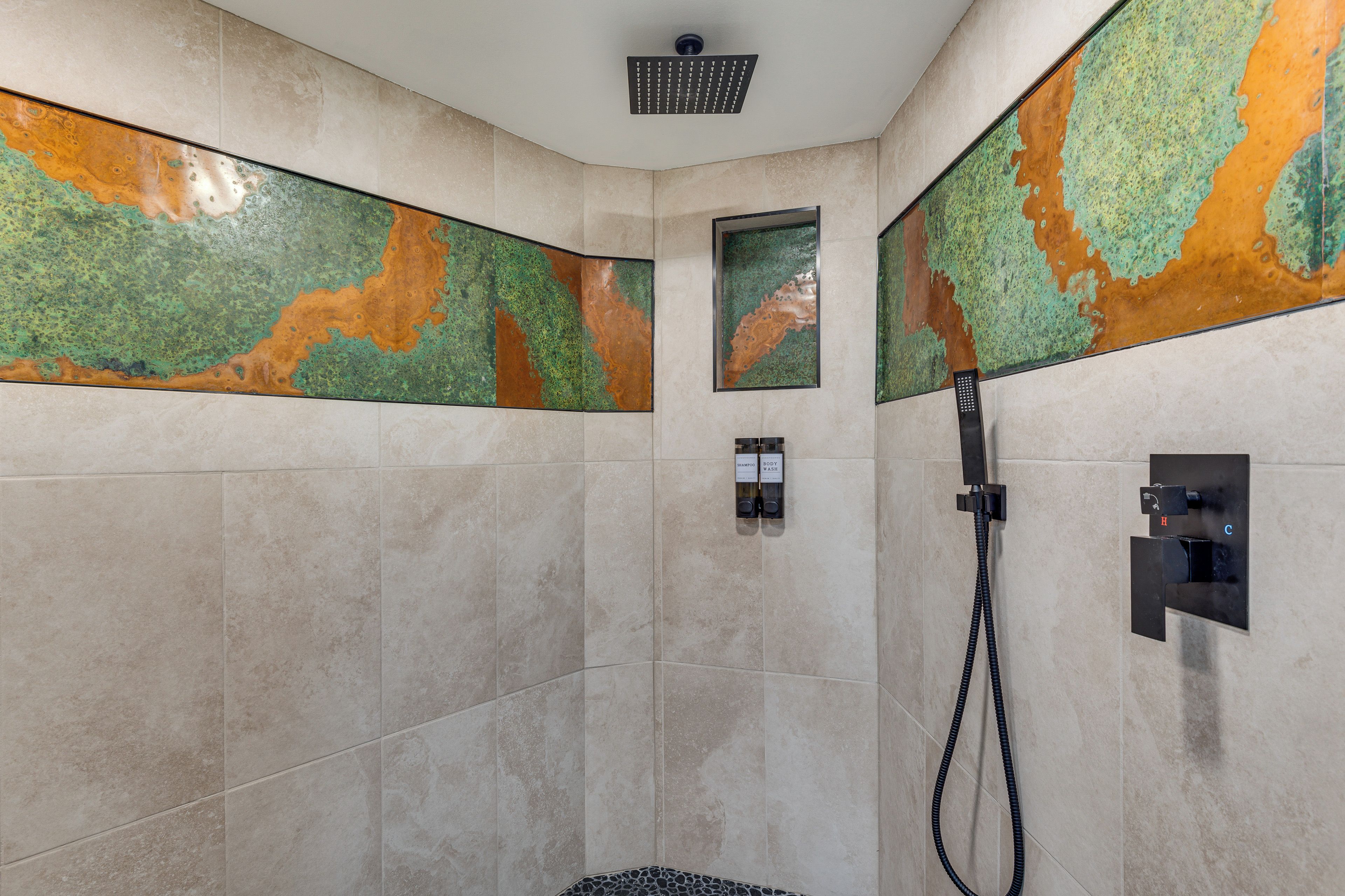 Zona de ducha con cabezal de ducha de lluvia, grifo de ducha de mano y panel de control en la pared con botones para diferentes funciones.