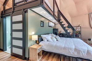 Un dormitorio con cama, mesita de noche, lámpara y una escalera que lleva a un nivel superior.