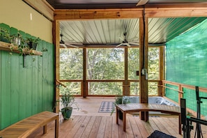 Una terraza de madera con un banco y un jacuzzi, rodeada por una valla verde y árboles.