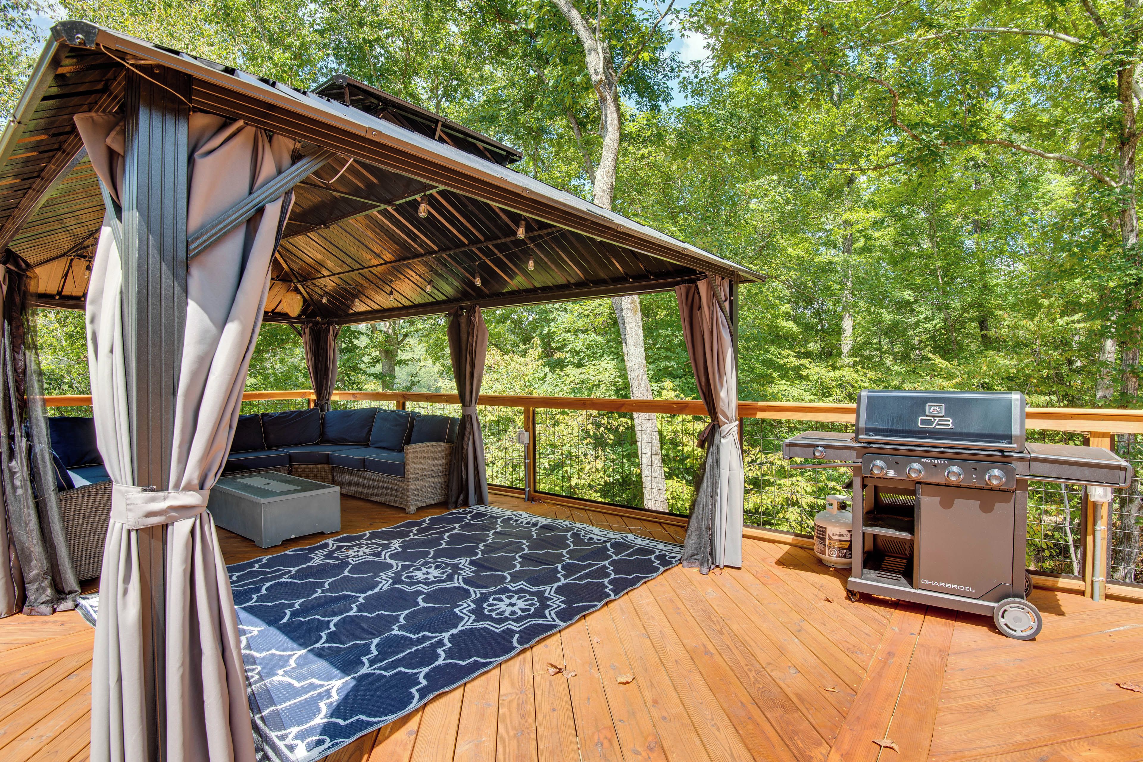 A covered outdoor seating area with a grill and a view of the forest.
