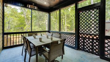 A covered outdoor seating area with a table and chairs, large windows, and a lattice screen.