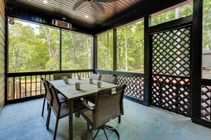 A covered outdoor seating area with a table and chairs, large windows, and a lattice screen.