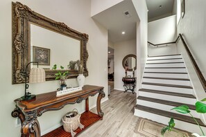 A hallway with a wooden console table, a mirror, a vase with plants, and a staircase.