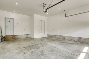 A spacious, well-lit garage with concrete flooring, two white doors, and a wooden step leading to a garage door.