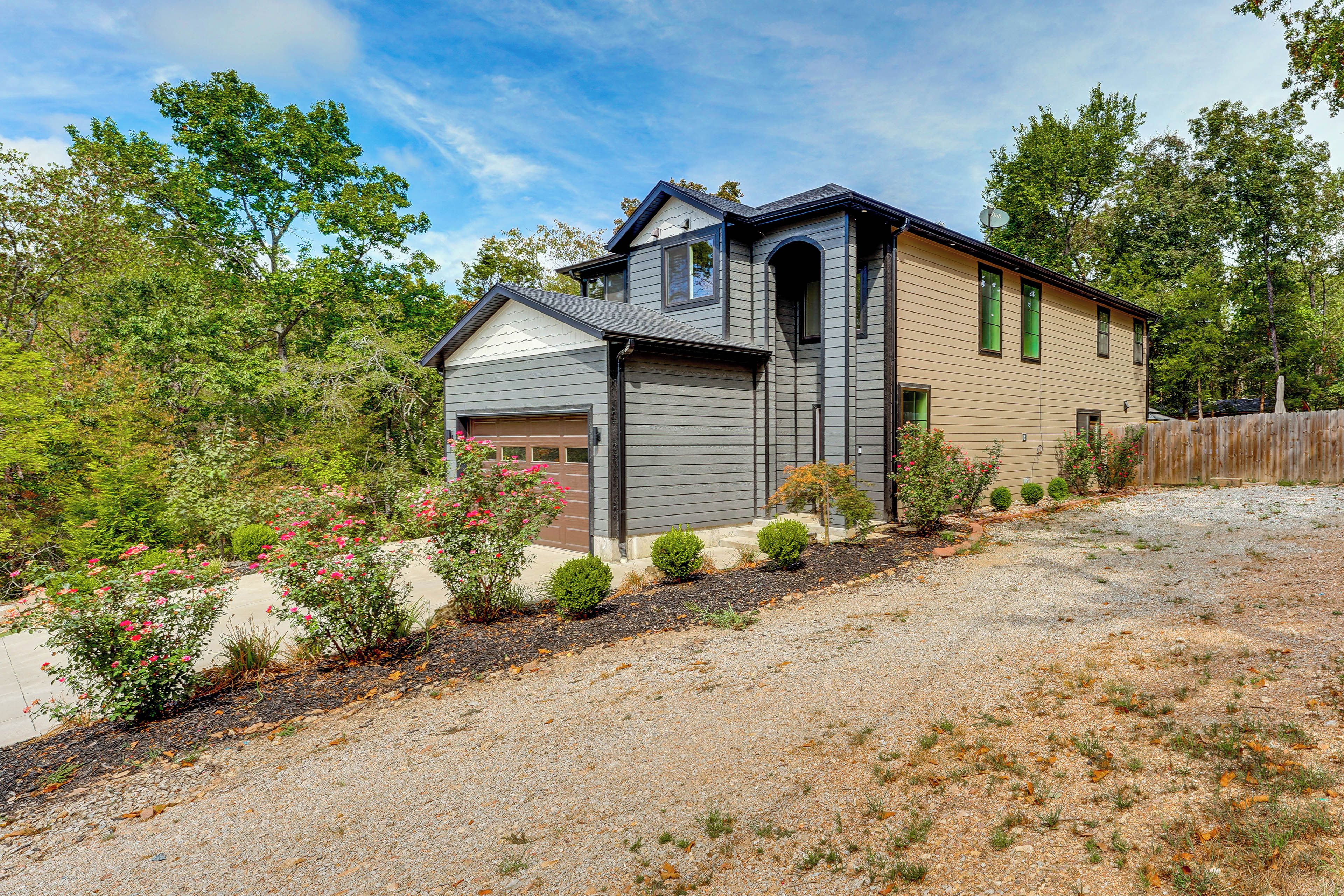A two-story house with a garage, surrounded by a gravel driveway and a wooden fence.