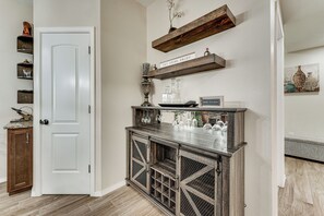 A hallway with a white door, a wooden cabinet with wine glasses, and a shelf with decorative items.