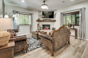 A living room with a fireplace, a sofa, a coffee table, and a television mounted above the fireplace.
