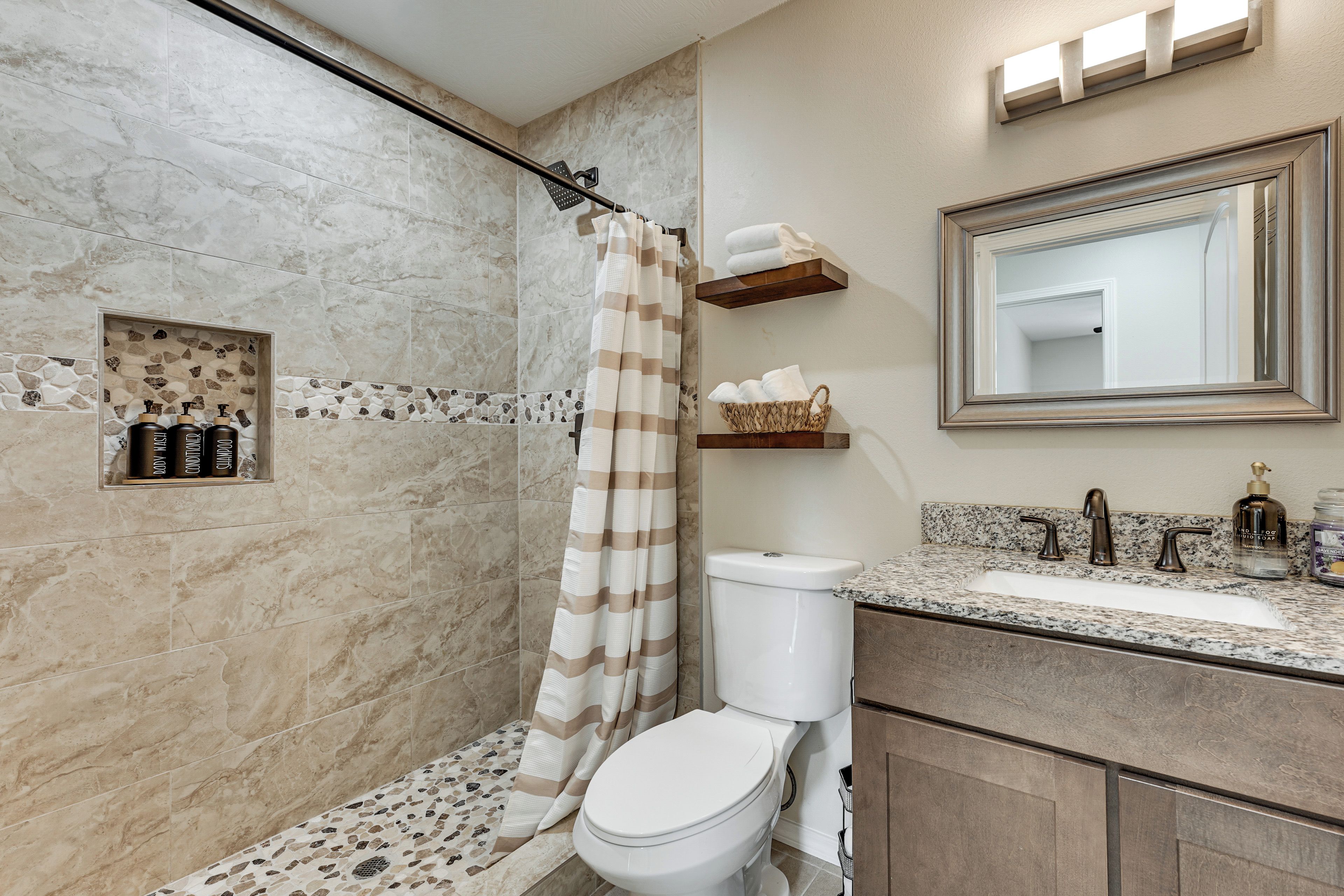 A bathroom with a shower, toilet, and sink. There are toiletries on the counter and a towel rack above the sink.