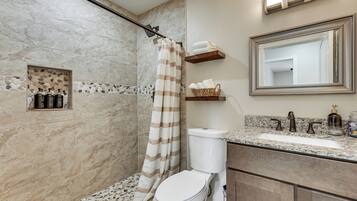 A bathroom with a shower, toilet, and sink. There are toiletries on the counter and a towel rack above the sink.