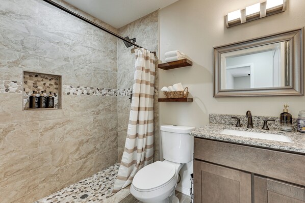 A bathroom with a shower, toilet, and sink. There are toiletries on the counter and a towel rack above the sink.