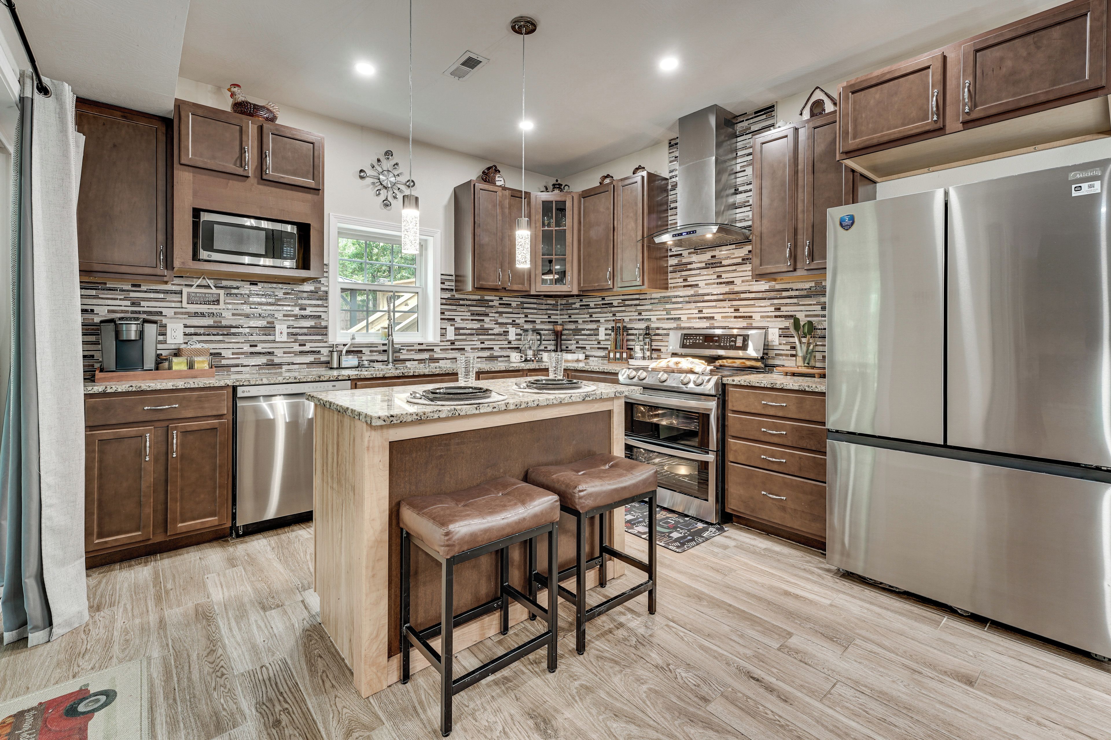 A modern kitchen with stainless steel appliances, wooden cabinets, and a central island with stools.