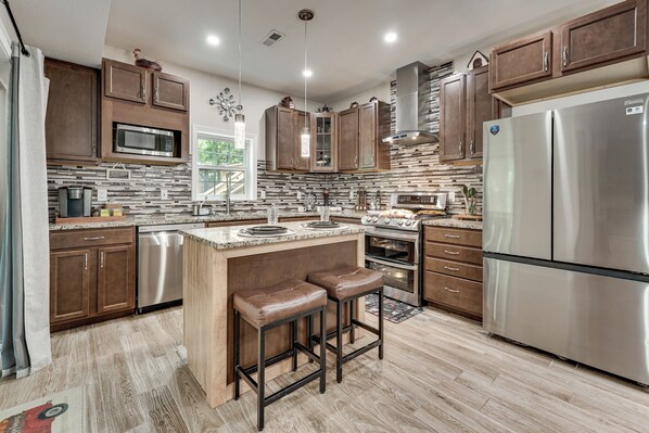 A modern kitchen with stainless steel appliances, wooden cabinets, and a central island with stools.
