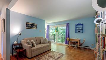 A living room with a sofa, a coffee table, a bookshelf, and a dining area with chairs and a table.