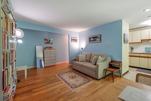 A living room with a sofa, a coffee table, and a bookshelf. There is a kitchen area with cabinets and a countertop. - 6 Mi to Uconn Health: Cozy Condo w/ Balcony (Farmington)