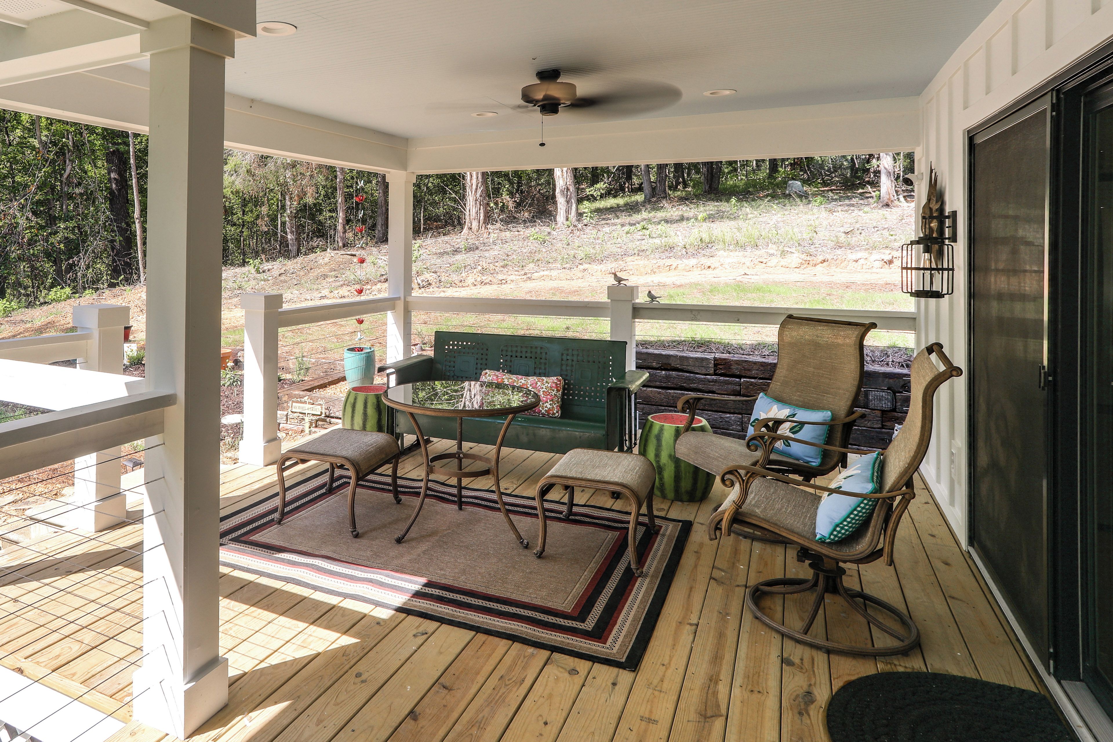 A covered outdoor seating area with a table and chairs, a sofa, and a view of the surrounding landscape.