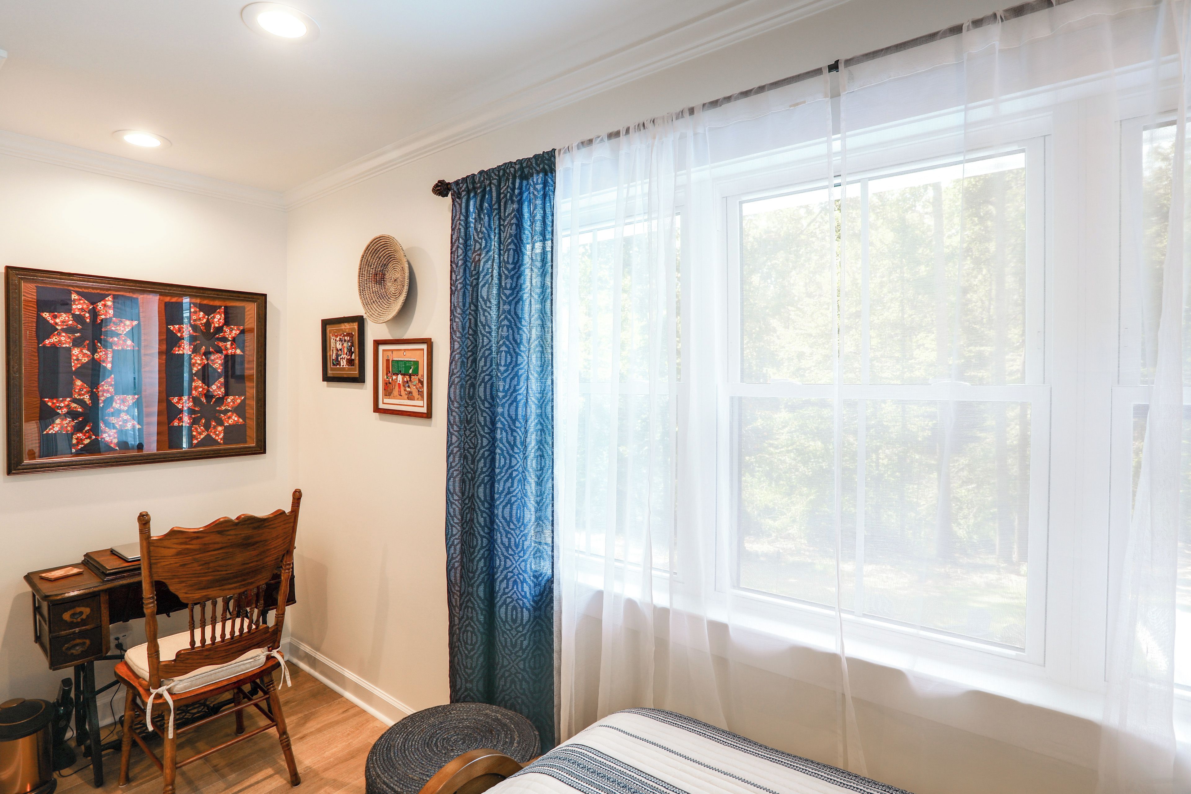 A room with a large window, a wooden chair, a small table, and wall decorations including framed artwork.