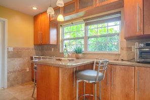 A kitchen with wooden cabinets, a large window with greenery outside, a bar area with stools, and a built-in oven. - Hot Tub, Water View! Largo Home 10 Mi to Beaches (Largo)
