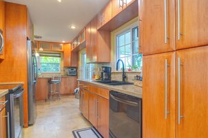 Una cocina con armarios de madera, un refrigerador de acero inoxidable, un lavamanos y un ventanal que proporciona luz natural.