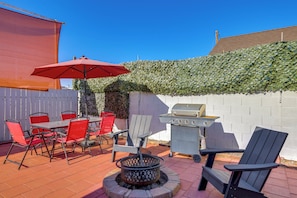 Un patio exterior con una parrilla, sillas rojas, una mesa y un hogar para la chimenea.