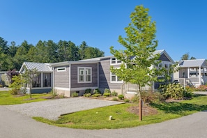 A modern two-story house with a grey and white exterior, a covered porch, and a well-maintained front yard with a gravel path and small shrubs.