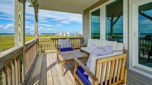 Um deck de madeira com sofá e cadeiras, com vista para uma paisagem verde e edifícios.