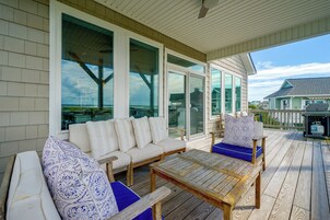 Un área de estar al aire libre techada con sofá y sillones, ventanas amplias y vista al océano.