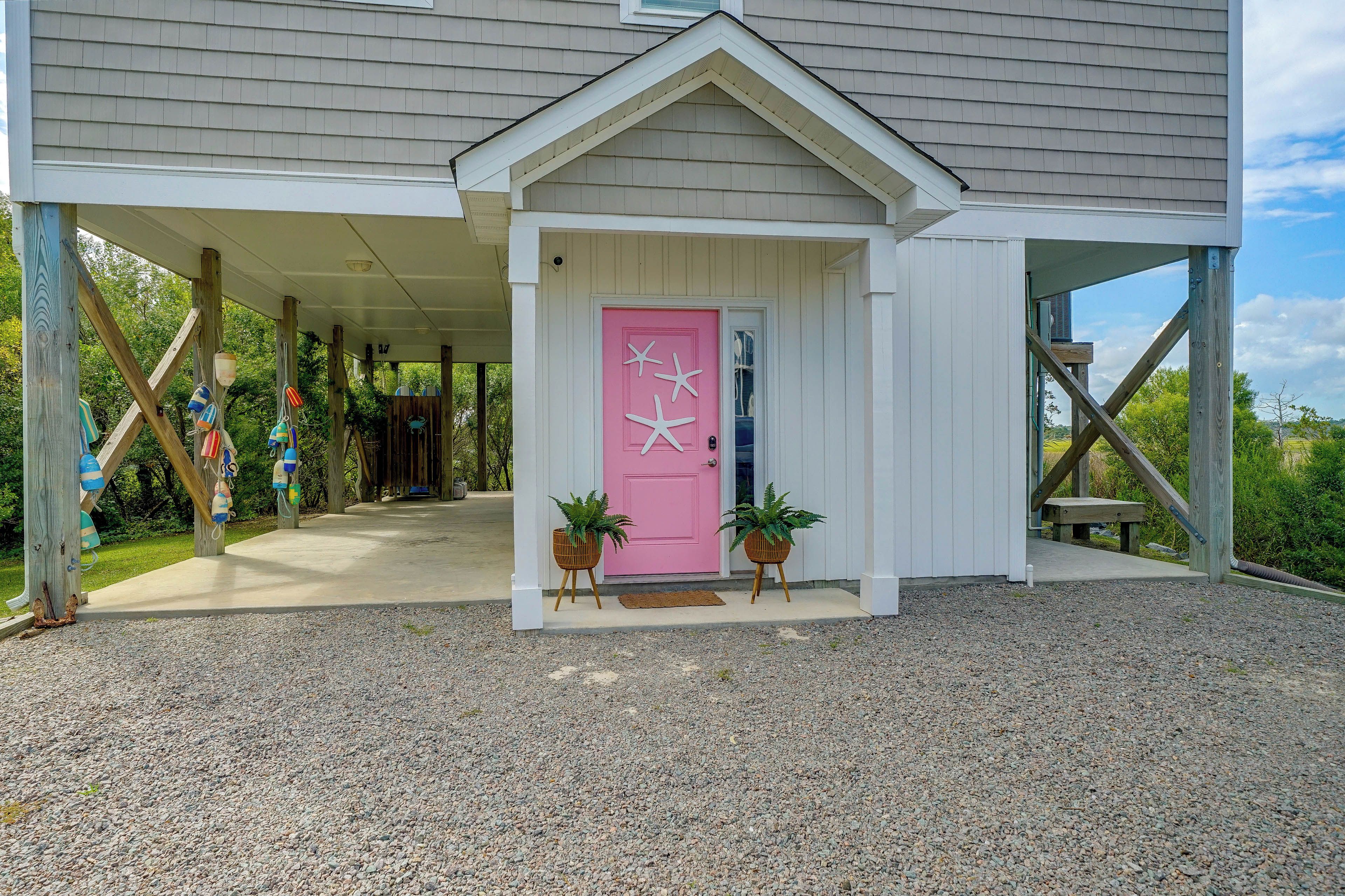 A house with a covered porch, a pink door with starfish decorations, and two potted plants.