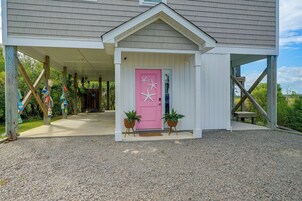Una casa con porche cubierto, una puerta rosa decorada con estrellas de mar y dos macetas con plantas.